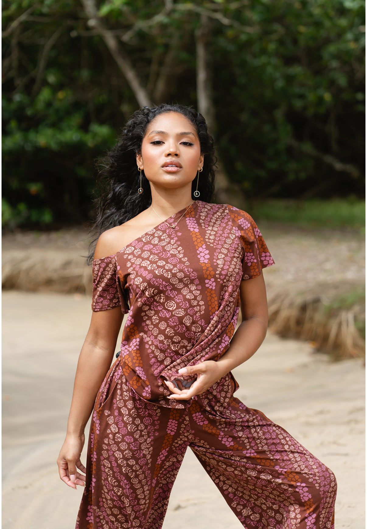 Woman wearing a patterned outfit standing outdoors with greenery in the background